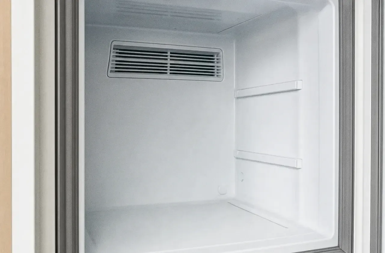 Empty white refrigeration compartment with a rear air vent and bare shelf rails